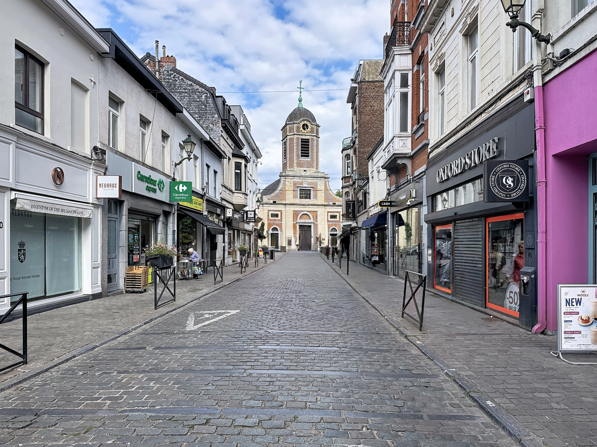 Rue commerçante pavée d'Uccle menant vers une église, ambiance de village animé