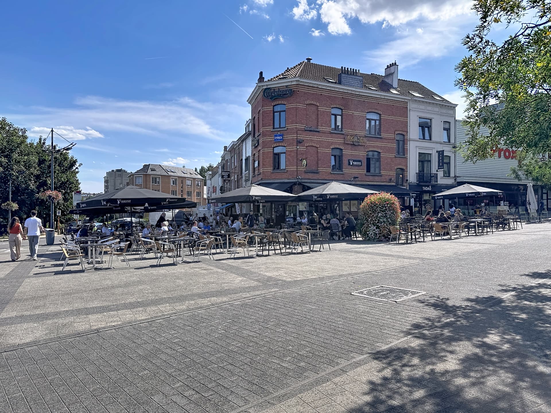 Terrasses animées place Georges Henri à Woluwe-Saint-Lambert, façades de café bordées d'arbres
