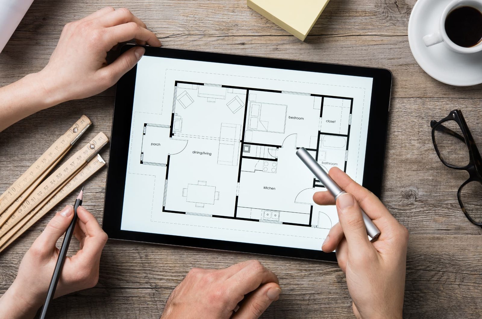 Plan d’un logement affiché sur une tablette, règle de mesure, stylet et tasse de café sur un bureau