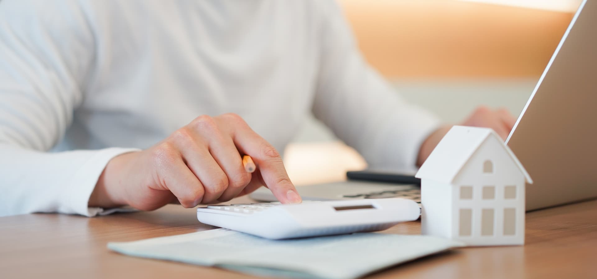 Calcul du coût d'un prêt immobilier avec une calculatrice, un ordinateur et une maquette de maison sur une table en bois