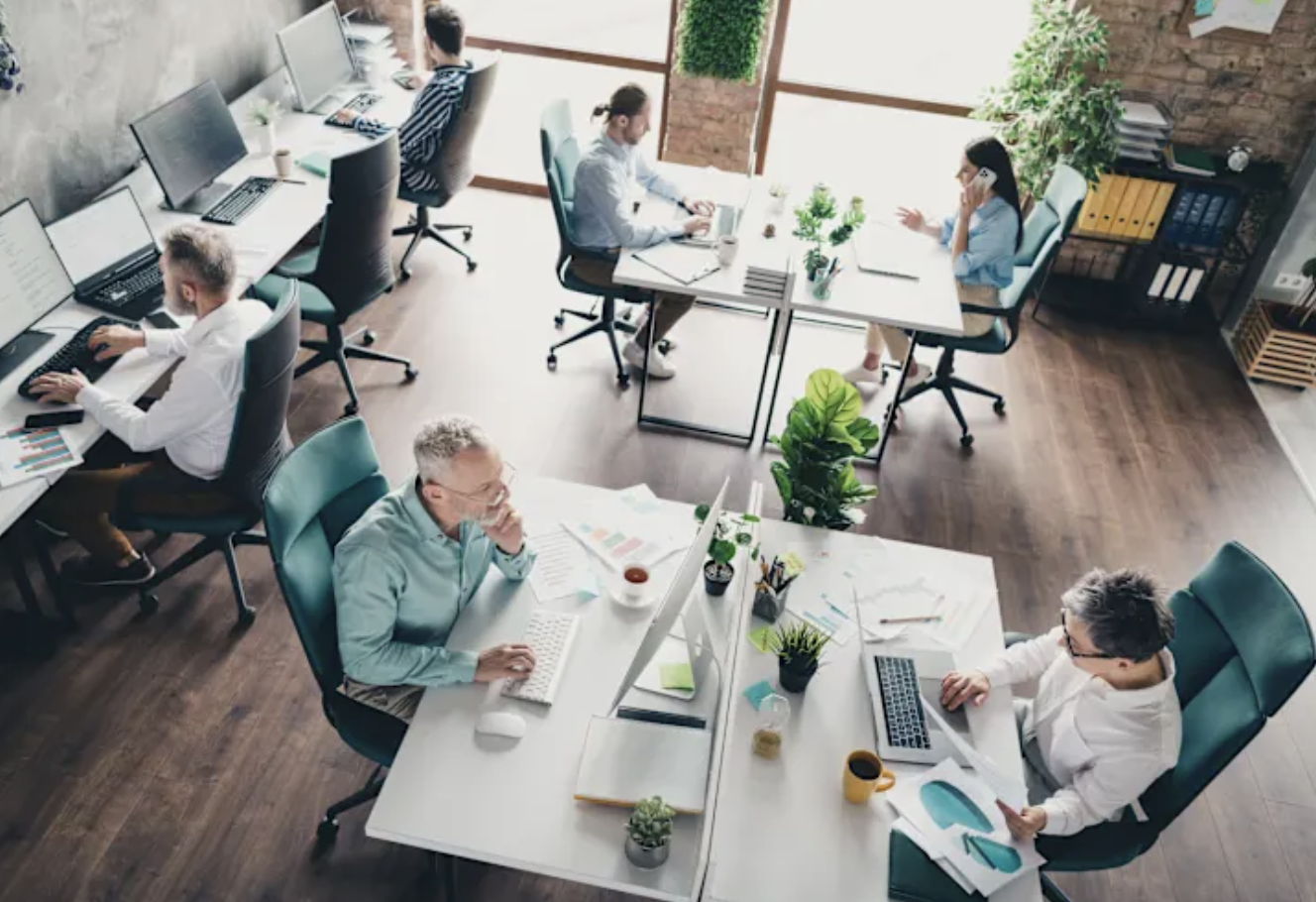 Espace de coworking lumineux avec personnes au travail, plantes et grandes fenêtres, dans un centre de bureaux flexibles à Bruxelles-Ville